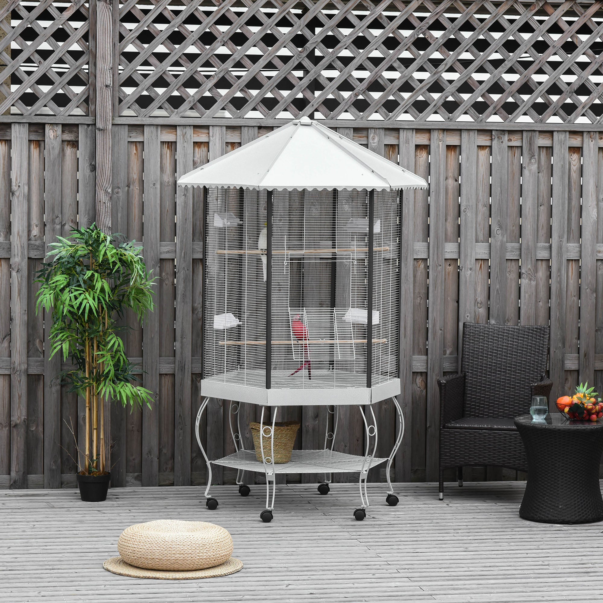 Outdoor setting with a birdcage, umbrella, and patio furniture against a wooden fence.